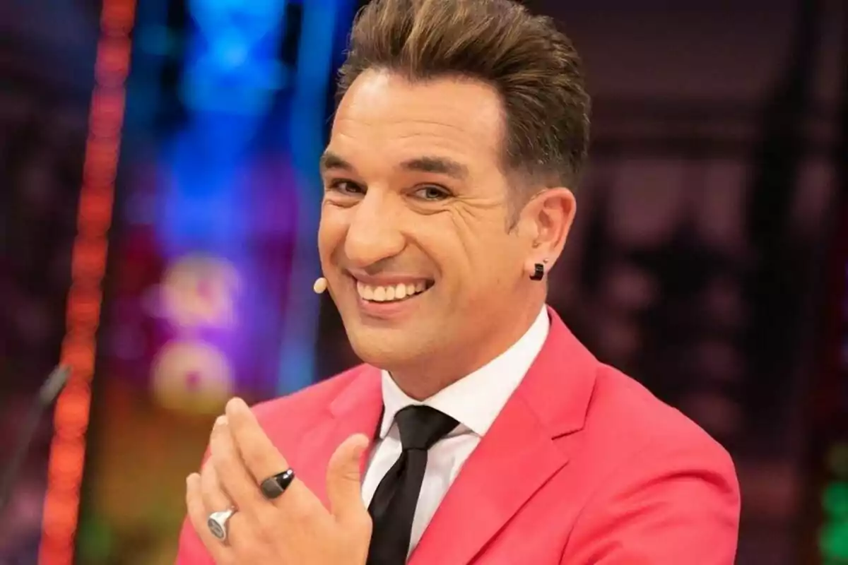 Miguel Lago somrient amb un vestit rosa i corbata negra en un ambient colorit a 'El Hormiguero'.
