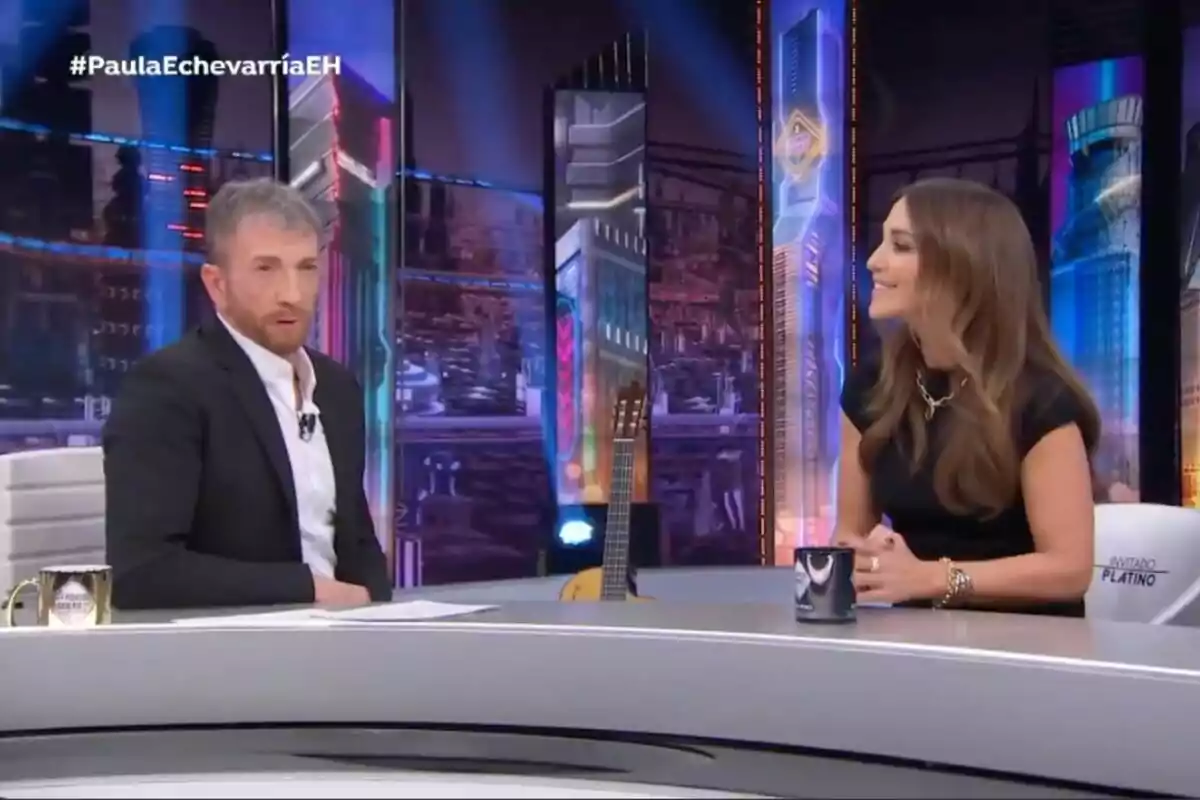 Pablo Motos y Paula Echevarría conversan en 'El Hormiguero' con una guitarra de fondo y una taza sobre la mesa.