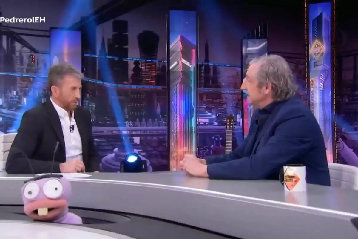 Pablo Motos y Josep Pedrerol conversan en 'El Hormiguero' con luces de neón y un fondo de ciudad, mientras una hormiga, Trancas, asoma en la parte inferior de la imagen. Pablo Motos y Josep Pedrerol conversan en 'El Hormiguero' con luces de neón y un fondo de ciudad, mientras una hormiga, Trancas, asoma en la parte inferior de la imagen.