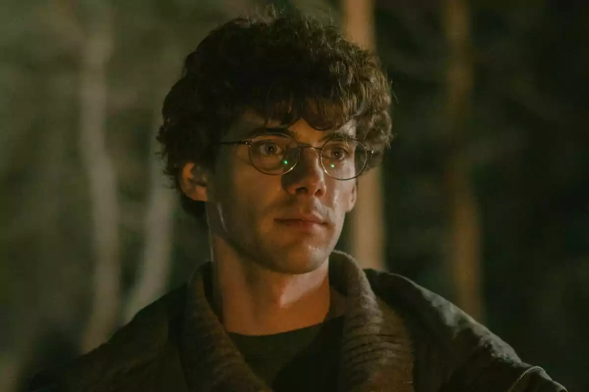 Álvaro Rico con gafas y cabello rizado mira hacia adelante en un entorno oscuro y arbolado en El Jardinero.
