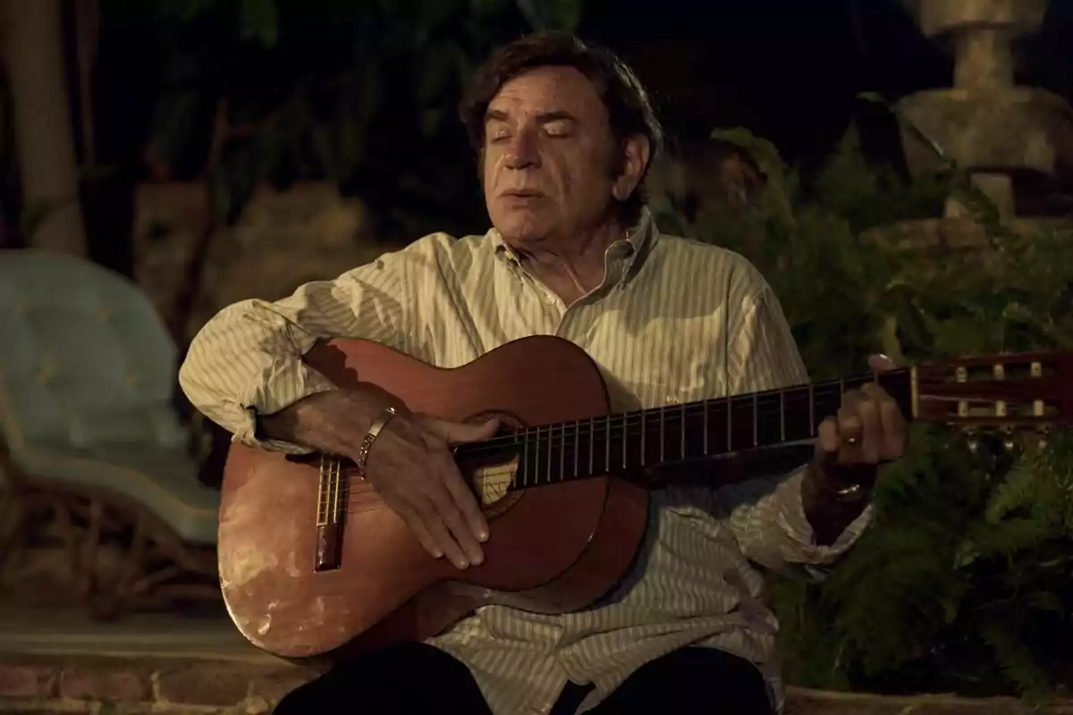 Un home gran tocant una guitarra acústica amb els ulls tancats en un entorn a l'aire lliure a la nit a la pel·lícula El Rey Peret Un home gran tocant una guitarra acústica amb els ulls tancats en un entorn a l'aire lliure a la nit a la pel·lícula El Rey Peret