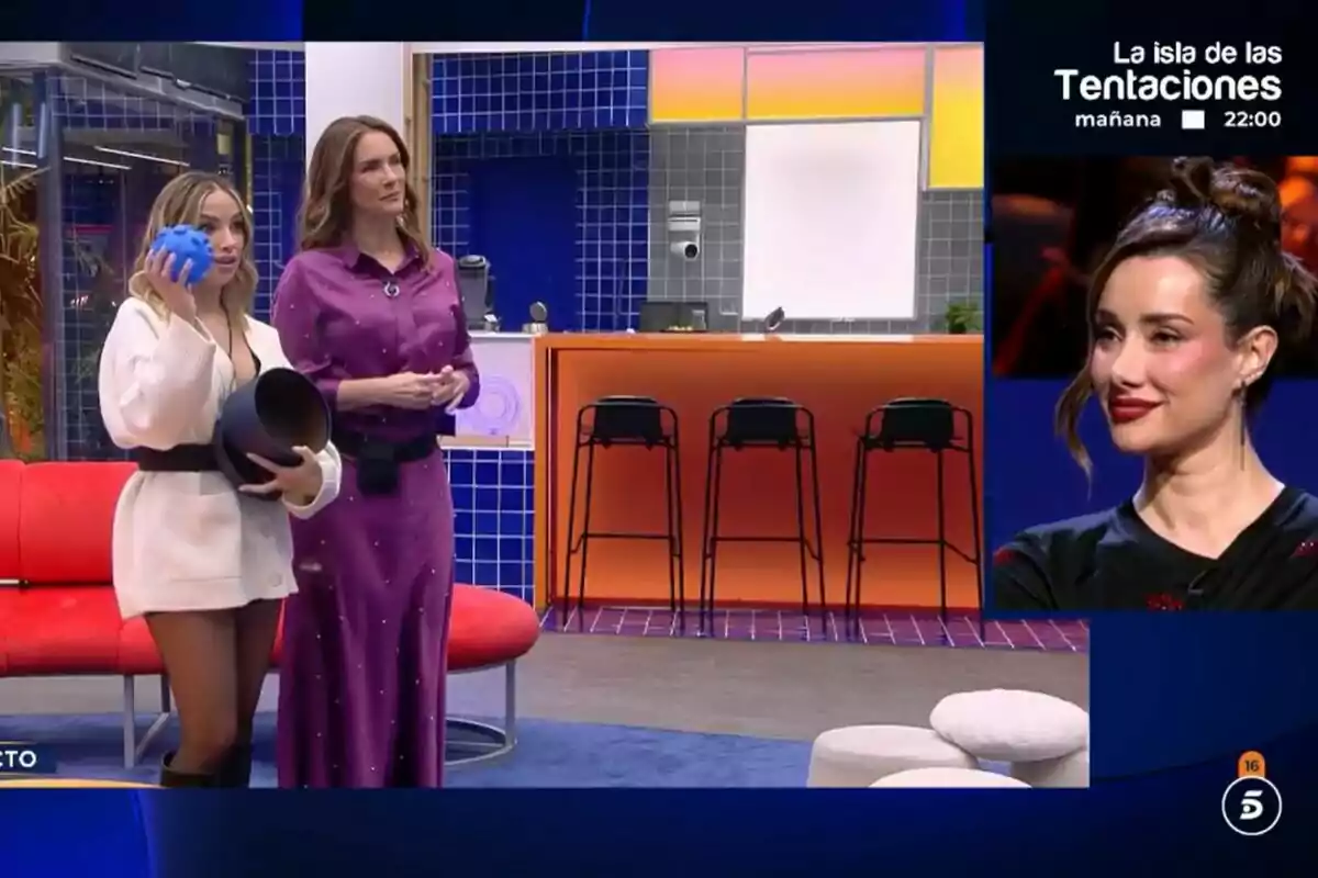Lucía Sánchez i Elena Rodríguez estan drets a la casa de GH DÚO, una sosté un objecte blau i un recipient negre i una imatge d'Adara Molinero somrient.