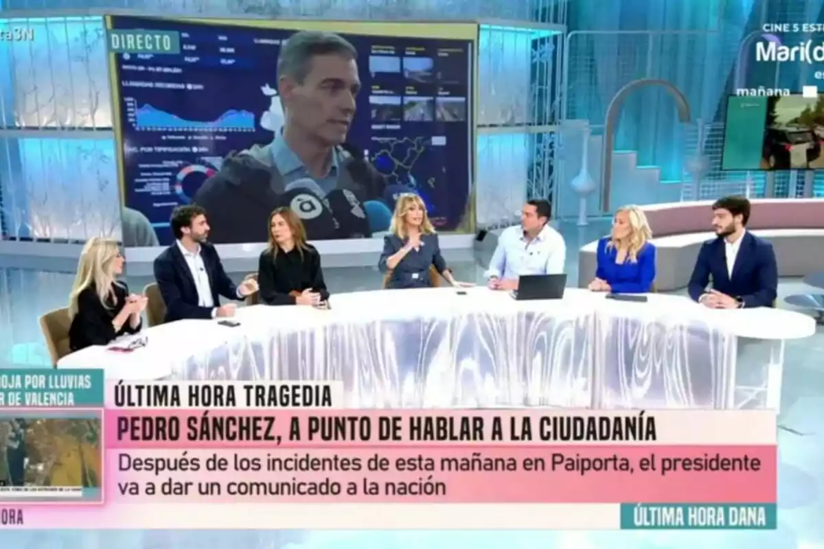 Un grupo de personas como Emma García o Cristina Cifuentes está sentado en una mesa de debate en Fiesta mientras en una pantalla grande se muestra a Pedro Sánchez en una transmisión en vivo. Un grupo de personas como Emma García o Cristina Cifuentes está sentado en una mesa de debate en Fiesta mientras en una pantalla grande se muestra a Pedro Sánchez en una transmisión en vivo.