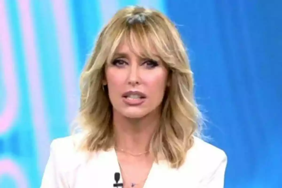 Emma García con cabello rubio y expresión seria en el plató de Fiesta con fondo azul. Emma García con cabello rubio y expresión seria en el plató de Fiesta con fondo azul.