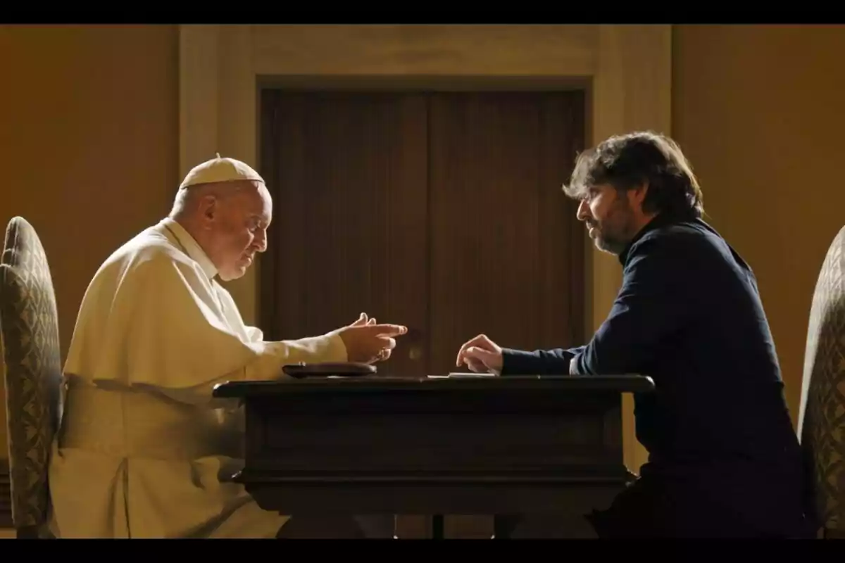 Papa Francesc i Jordi Évole asseguts cara a cara en una taula, un d'ells vestit amb indumentària religiosa blanca, conversen en una habitació il·luminada.