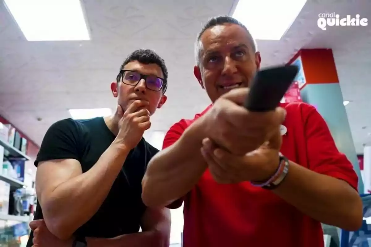 César Toral (Escaleto) y Victor Sandoval observan atentamente mientras uno de ellos sostiene un control remoto en una tienda, con el logo de César Toral (Escaleto) y Victor Sandoval observan atentamente mientras uno de ellos sostiene un control remoto en una tienda, con el logo de