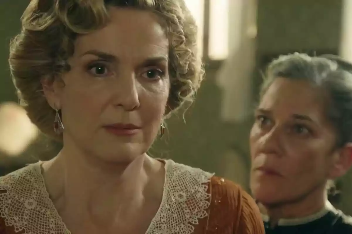 Dos mujeres en una escena dramática de 'La Promesa', una de ellas es la actriz Eva Martín con expresión seria y la otra observándola desde atrás. Dos mujeres en una escena dramática de 'La Promesa', una de ellas es la actriz Eva Martín con expresión seria y la otra observándola desde atrás.