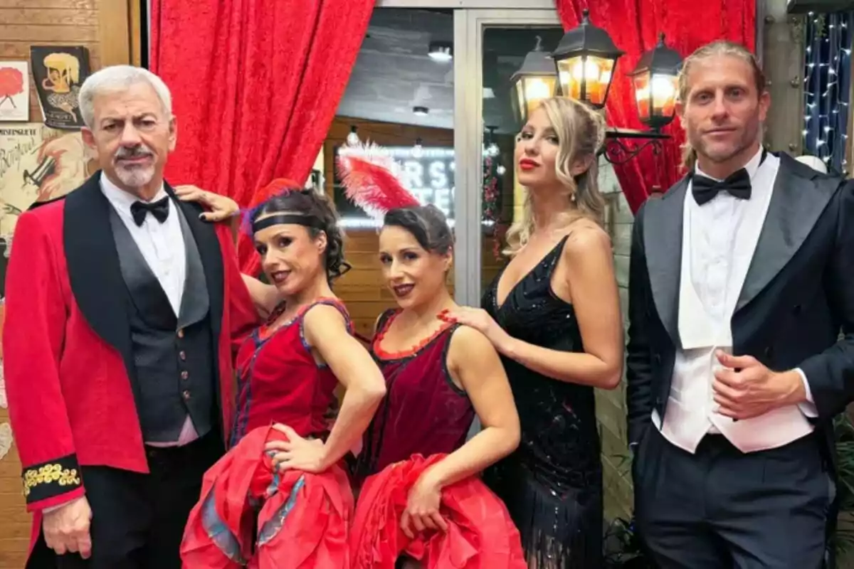 Un grup de persones vestides com Carlos Sobera amb vestits elegants i d'època posen davant d'un fons decorat amb cortines vermelles i llums a la nit de Cap d'Any de First Dates. Un grup de persones vestides com Carlos Sobera amb vestits elegants i d'època posen davant d'un fons decorat amb cortines vermelles i llums a la nit de Cap d'Any de First Dates.