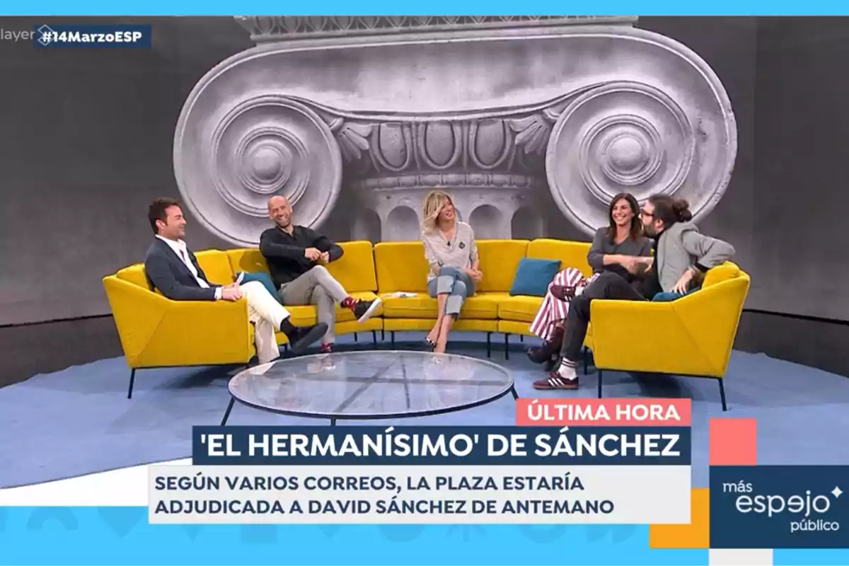 Un grup de persones està assegut en un sofà groc en un plató de televisió, conversant i somrient, amb un fons que mostra un disseny arquitectònic clàssic. Captura de 'Espejo Público'. Un grup de persones està assegut en un sofà groc en un plató de televisió, conversant i somrient, amb un fons que mostra un disseny arquitectònic clàssic. Captura de 'Espejo Público'.