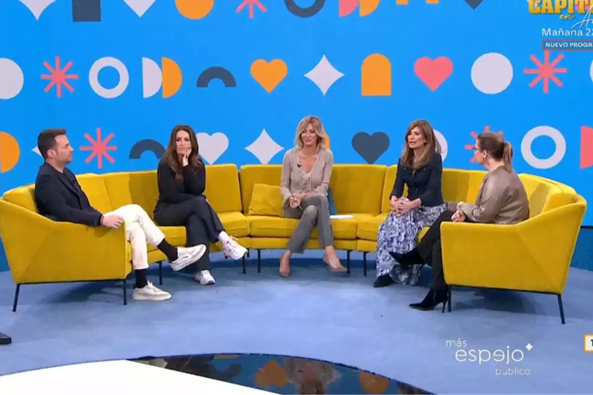 Un grup de persones està assegut en un sofà groc en un plató de televisió amb un fons blau decorat amb formes geomètriques acolorides. Captura de 'Espejo Público'.