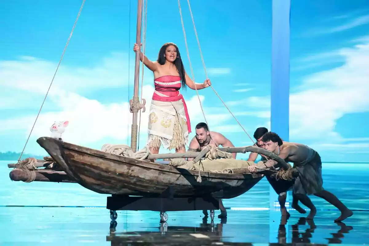 Esperansa Grasia disfrazada de Moana está de pie en una balsa mientras tres hombres la empujan en un escenario con fondo de mar y cielo azul en Tu Cara Me Suena Esperansa Grasia disfrazada de Moana está de pie en una balsa mientras tres hombres la empujan en un escenario con fondo de mar y cielo azul en Tu Cara Me Suena