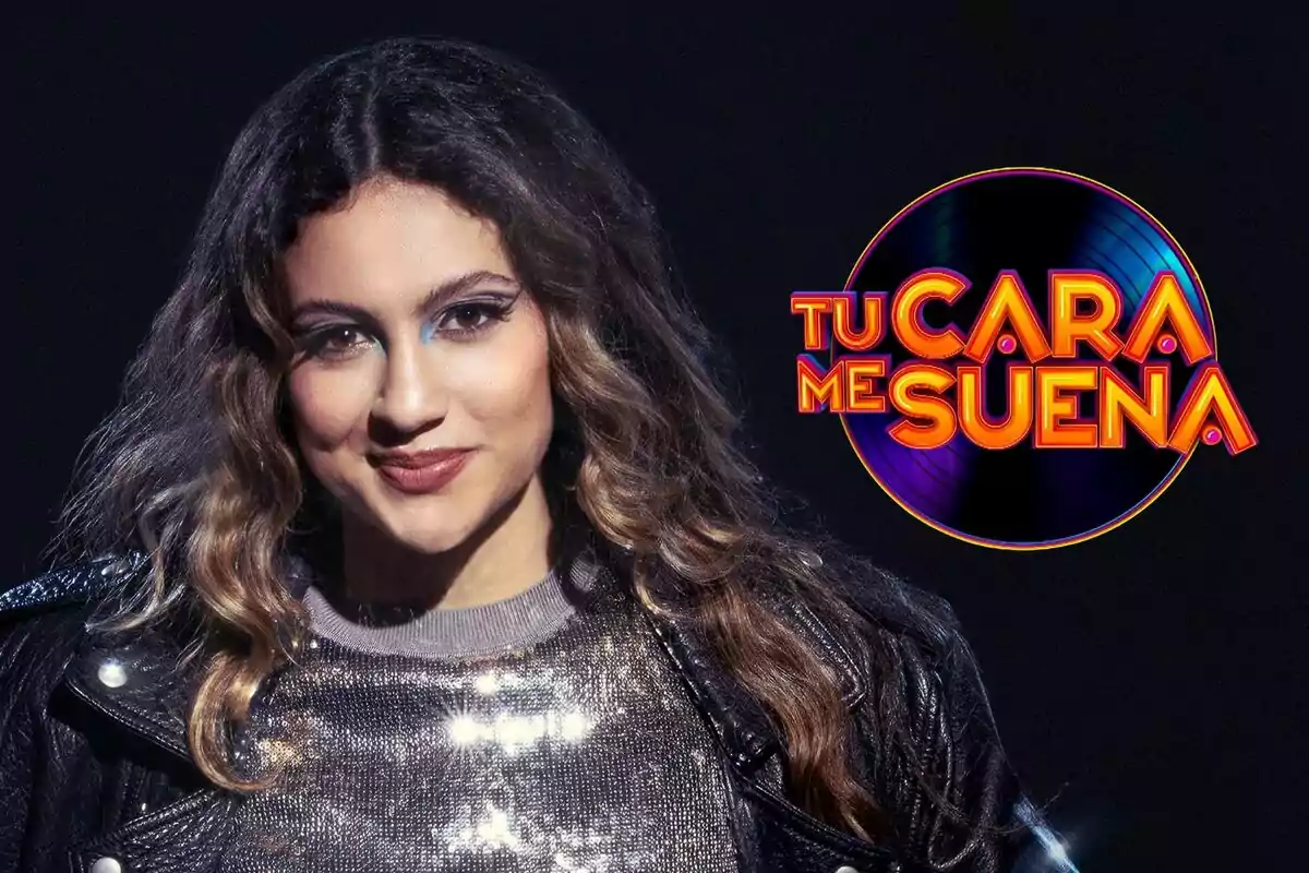 Esperansa Grasia con cabello rizado y maquillaje llamativo, vestida con una chaqueta de cuero y un suéter brillante, junto al logo del programa "Tu Cara Me Suena".