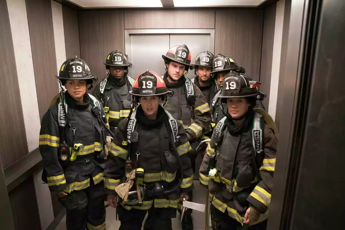 Un grupo de bomberos con uniformes completos y cascos numerados con el número 19 están dentro de un ascensor, listos para una misión de la serie Estación 19 Un grupo de bomberos con uniformes completos y cascos numerados con el número 19 están dentro de un ascensor, listos para una misión de la serie Estación 19