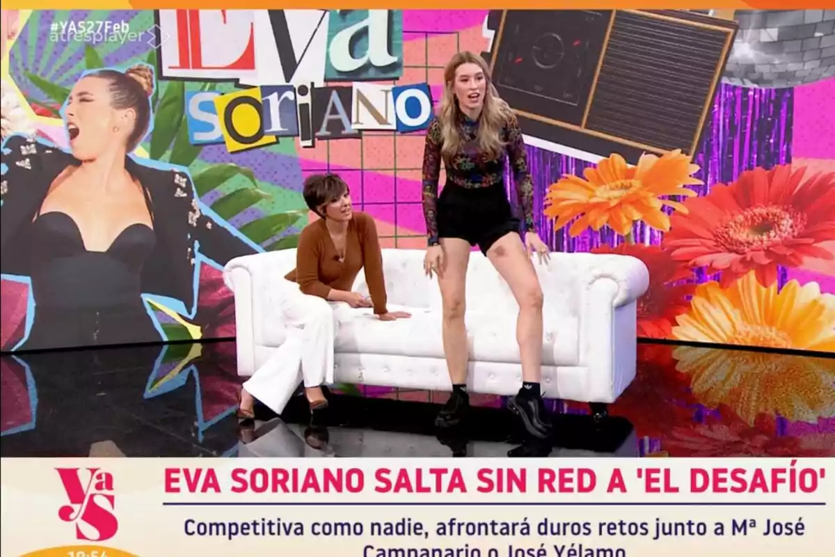 En un colorido set de televisión, Eva Soriano y Sonsoles Ónega interactúan mientras una de ellas está de pie y la otra sentada en un sofá blanco, con un fondo vibrante que incluye flores y un collage de letras. En un colorido set de televisión, Eva Soriano y Sonsoles Ónega interactúan mientras una de ellas está de pie y la otra sentada en un sofá blanco, con un fondo vibrante que incluye flores y un collage de letras.