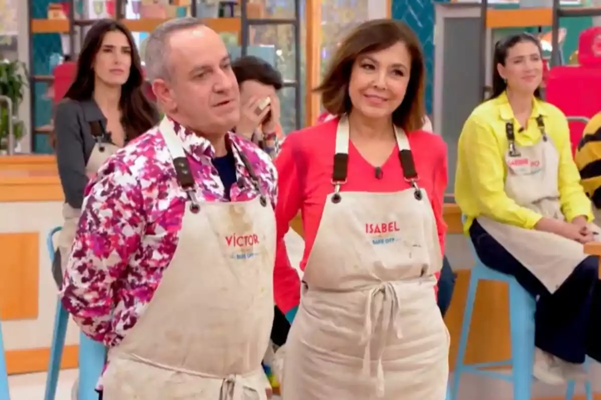 Víctor Sandoval i Isabel Gemio amb davantals en un plató de cuina, un d'ells porta una camisa acolorida i l'altre un jersei vermell a 'Bake Off: Famosos al forn'.