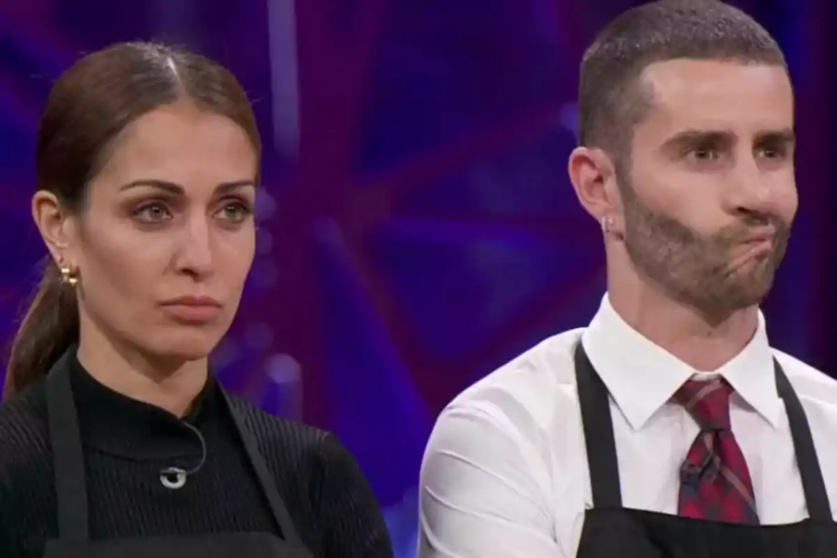 Hiba Abouk y Pelayo Díaz con delantales negros en MasterChef Celebrity con expresiones serias. Hiba Abouk y Pelayo Díaz con delantales negros en MasterChef Celebrity con expresiones serias.