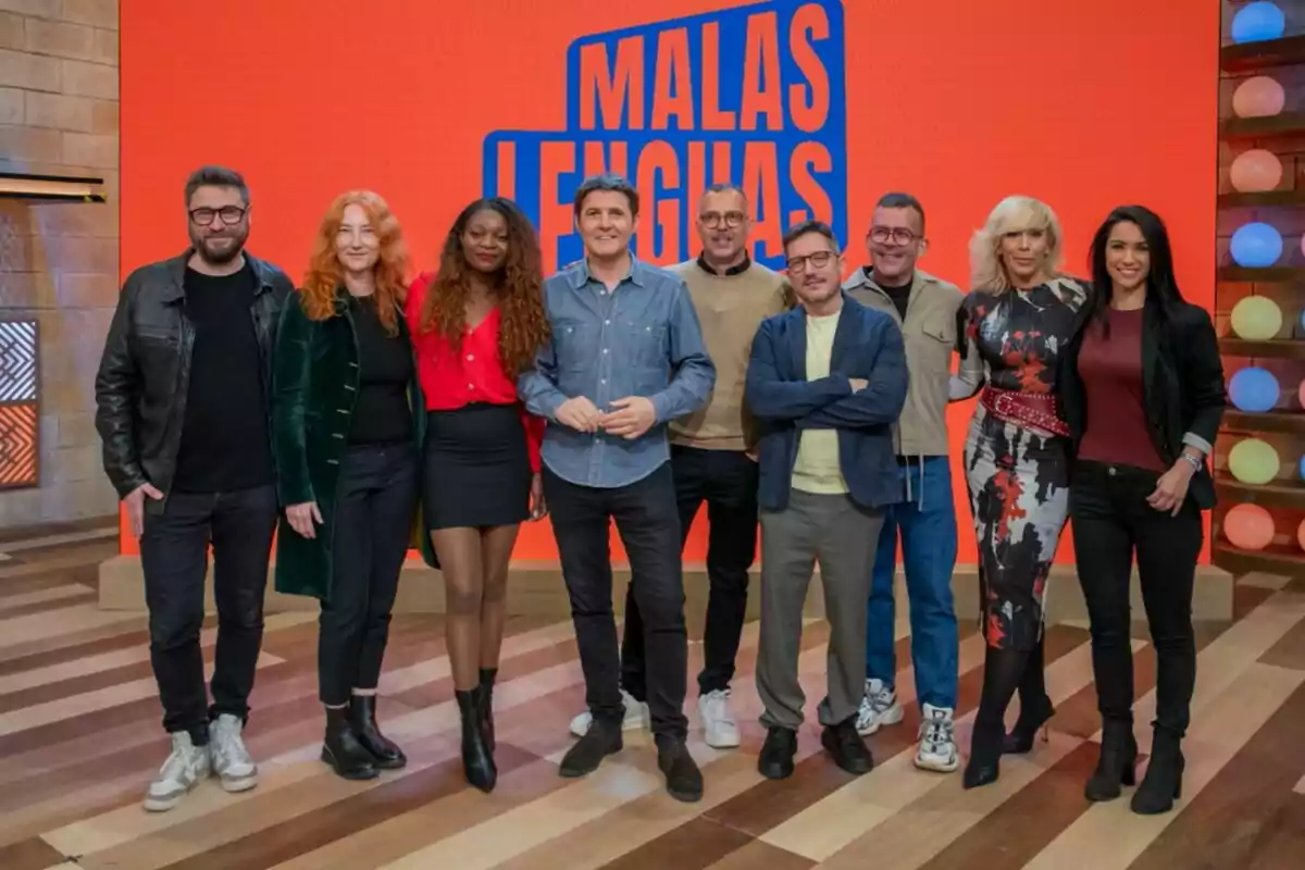 Un grup de persones posant juntes en un plató de televisió amb un fons taronja que té el text Un grup de persones posant juntes en un plató de televisió amb un fons taronja que té el text