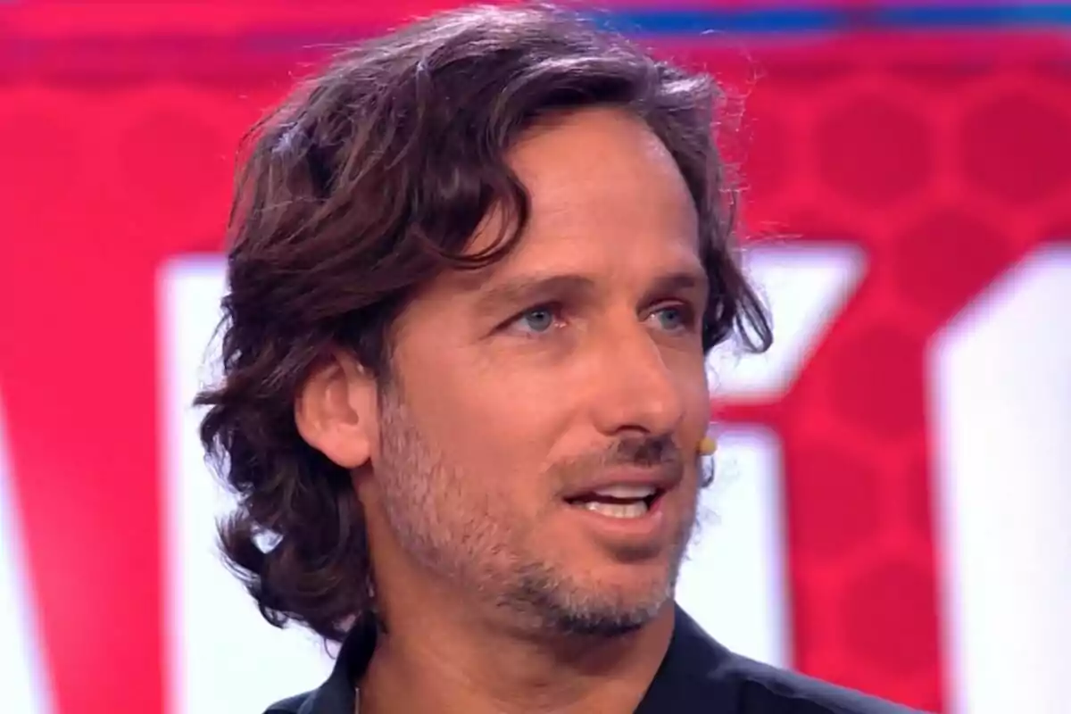 Feliciano López con cabello castaño y barba ligera hablando en un programa de televisión con fondo rojo en El Desafío.