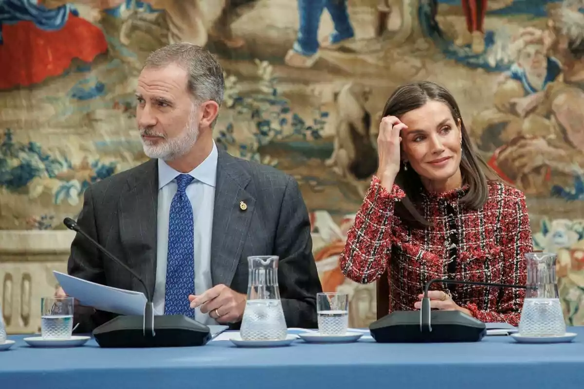 Felipe VI mirando a un lado serio en traje gris y corbata azul y Letizia mirando al otro sonriendo con la mano en la cabeza y una chaqueta de cuadros de colores Felipe VI mirando a un lado serio en traje gris y corbata azul y Letizia mirando al otro sonriendo con la mano en la cabeza y una chaqueta de cuadros de colores