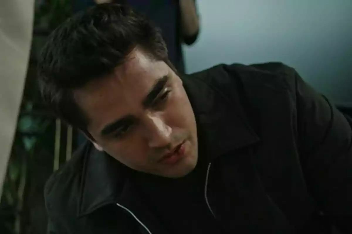 Ferit con expresión seria y chaqueta oscura mira hacia abajo en un entorno interior en Una nueva vida.