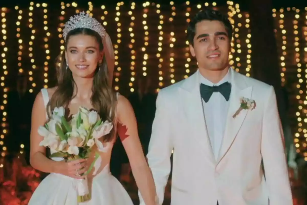Una pareja formada por Ferit y Seyran vestida de novios sonríe mientras camina de la mano en un ambiente iluminado con luces brillantes en Una nueva vida.