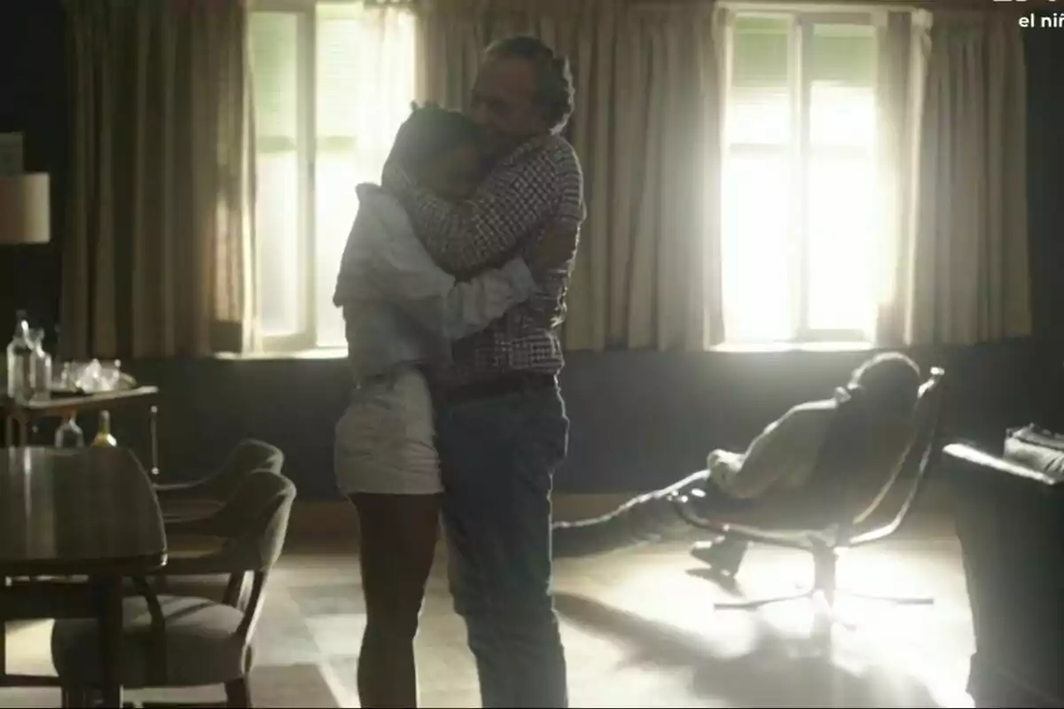 José Coronado y Nona Sobo se abrazan en una habitación iluminada por la luz que entra por una ventana, mientras otra persona está sentada en una silla al fondo, en el final de Entrevías. José Coronado y Nona Sobo se abrazan en una habitación iluminada por la luz que entra por una ventana, mientras otra persona está sentada en una silla al fondo, en el final de Entrevías.
