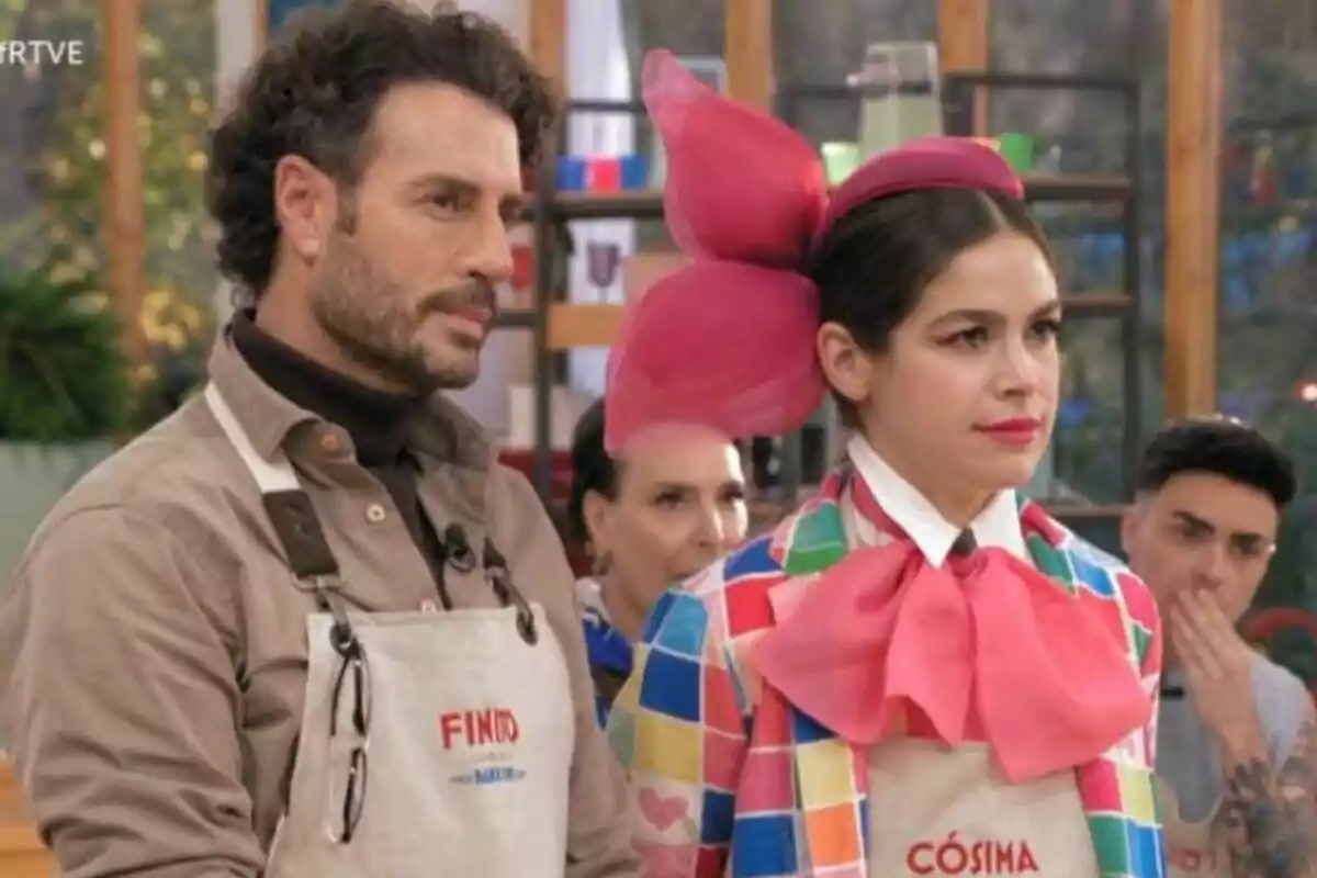 Finit de Còrdova i Cósima Ramírez amb davantals a Bake Off: famosos al forn, una porta un vestit colorit amb un gran llaç rosa al cap.