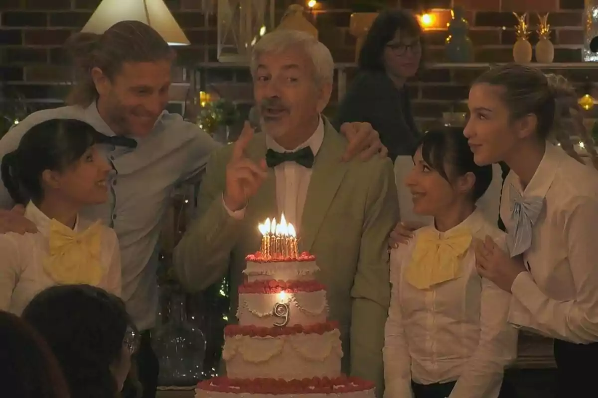 Un grupo de personas liderado por Carlos Sobera sonríe alrededor de un pastel de cumpleaños con velas encendidas en un ambiente festivo en First Dates.