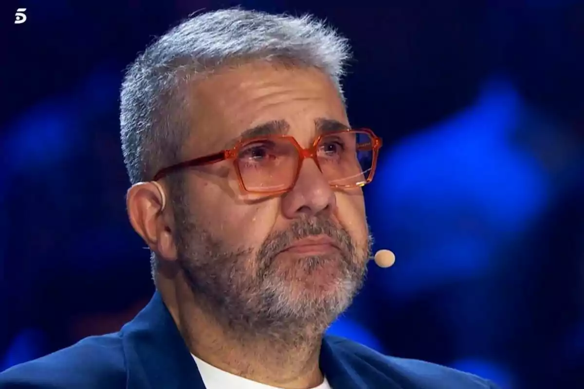 Florentino Fernández con gafas naranjas y barba gris parece emocionado mientras está en un escenario iluminado en Got Talent. Florentino Fernández con gafas naranjas y barba gris parece emocionado mientras está en un escenario iluminado en Got Talent.