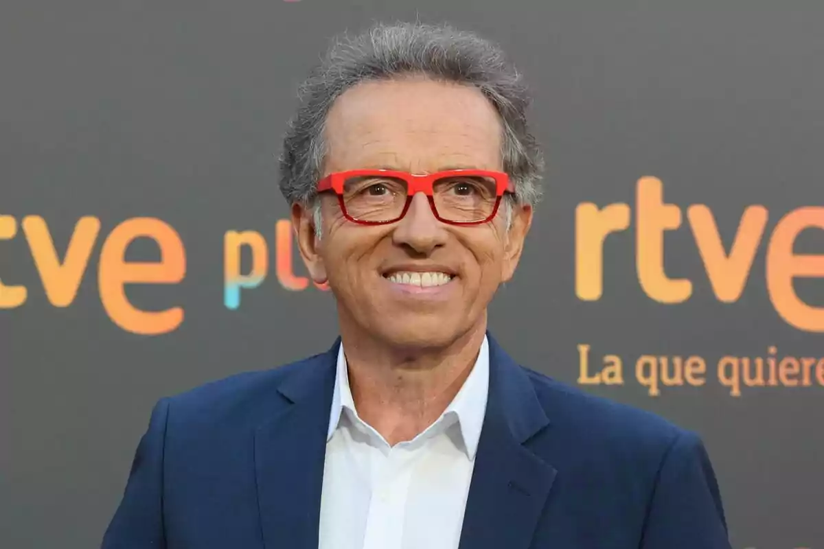 Foto de Jordi Hurtado en primer plano, mirando a cámara, sonriendo y usando un traje con unas gafas de color rojo