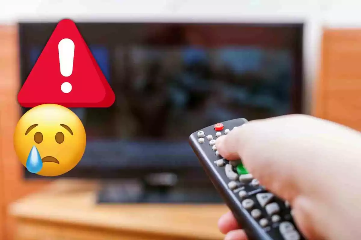 Una mà sosté un control remot apuntant a un televisor apagat amb un emoji d'advertència i un emoji trist superposats.
