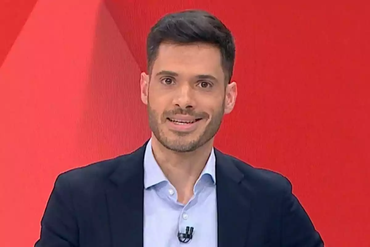 Fran López Galán con barba y cabello oscuro lleva un traje oscuro y camisa clara mientras sonríe frente a un fondo rojo en laSexta Noticias.