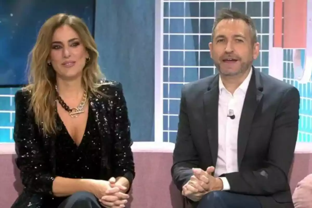 Verónica Dulanto y Frank Blanco sentados en Fiesta, una mujer con chaqueta negra brillante y un hombre con traje oscuro. Verónica Dulanto y Frank Blanco sentados en Fiesta, una mujer con chaqueta negra brillante y un hombre con traje oscuro.