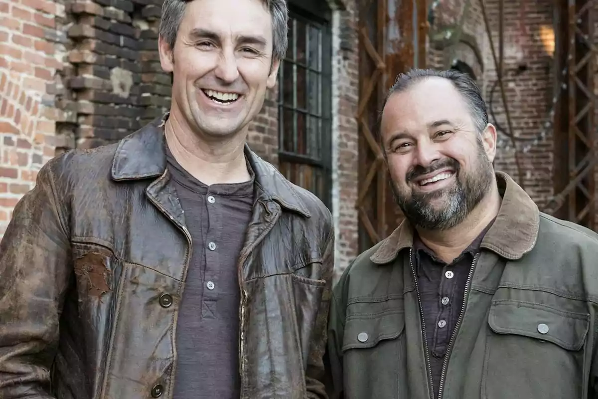 Frank Fritz y Mike Wolfe sonrientes posan frente a un edificio de ladrillos. Frank Fritz y Mike Wolfe sonrientes posan frente a un edificio de ladrillos.