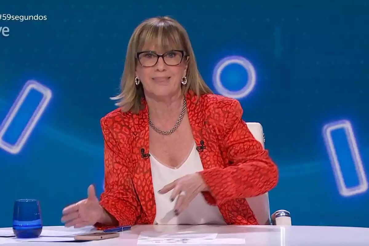Gemma Nierga con gafas y chaqueta roja está sentada en un estudio de televisión de 59 segundos con fondo azul. Gemma Nierga con gafas y chaqueta roja está sentada en un estudio de televisión de 59 segundos con fondo azul.