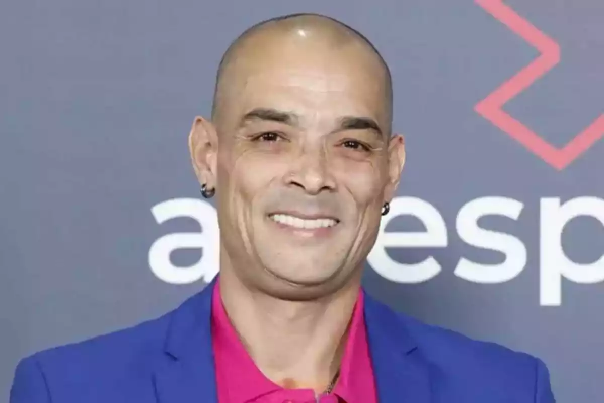 Gervasio Deferr calvo sonriendo con un traje azul y camisa rosa frente a un fondo gris.