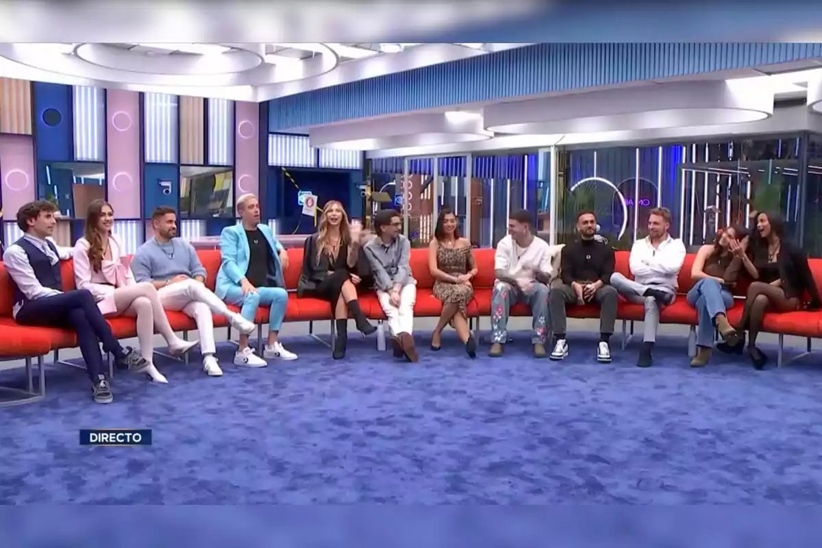 Un grupo de personas sentadas en un sofá rojo en un estudio de televisión con una decoración moderna y colorida. Captura de 'GH Dúo'