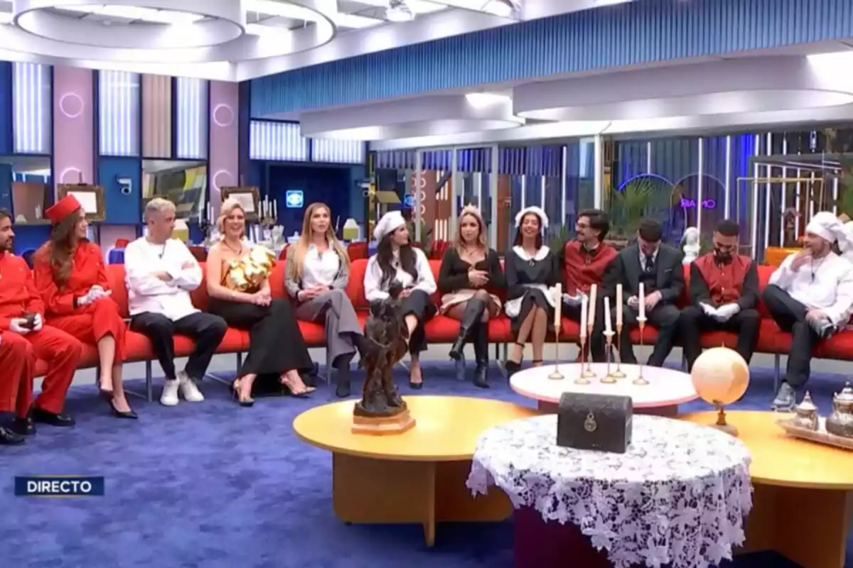 Un grupo de personas está sentado en un sofá rojo en un estudio de televisión decorado con luces y muebles modernos, algunas personas llevan disfraces temáticos. Captura de 'GH Dúo' Un grupo de personas está sentado en un sofá rojo en un estudio de televisión decorado con luces y muebles modernos, algunas personas llevan disfraces temáticos. Captura de 'GH Dúo'