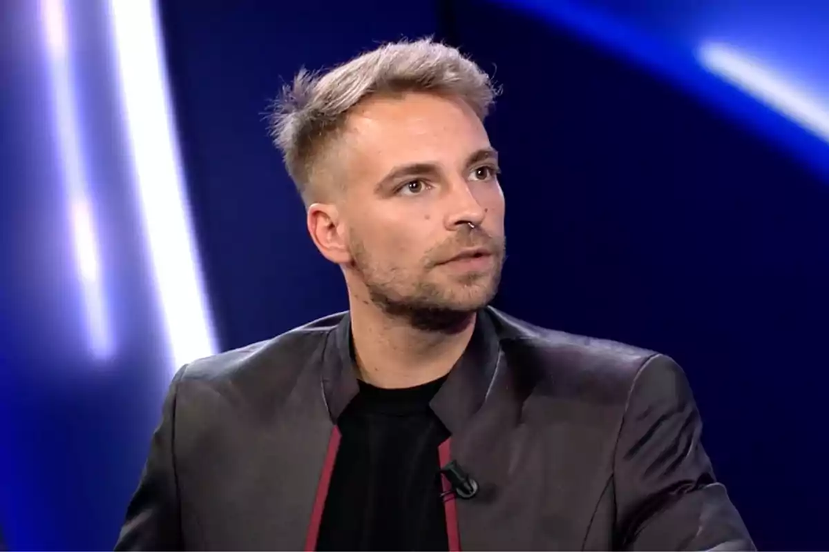 José María Almoguera con chaqueta oscura y cabello corto rubio está sentado en un estudio de televisión con luces azules de fondo. Captura de 'GH Dúo' José María Almoguera con chaqueta oscura y cabello corto rubio está sentado en un estudio de televisión con luces azules de fondo. Captura de 'GH Dúo'