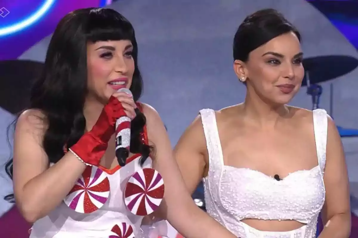 Gisela i Chenoa en un escenari, una d'elles sosté un micròfon i porta un vestit amb disseny de caramels, mentre que l'altra va vestida de blanc i ambdues semblen estar participant a Tu Cara Me Suena.