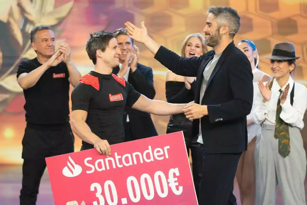 Un grupo de personas aplaude mientras Roberto Leal entrega un cheque grande a Gotzon Mantuliz en El Desafío. Un grupo de personas aplaude mientras Roberto Leal entrega un cheque grande a Gotzon Mantuliz en El Desafío.