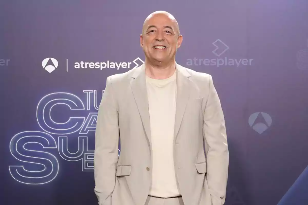 Goyo Jiménez calvo con traje claro sonríe frente a un fondo con logotipos de Atresplayer y Goyo Jiménez calvo con traje claro sonríe frente a un fondo con logotipos de Atresplayer y