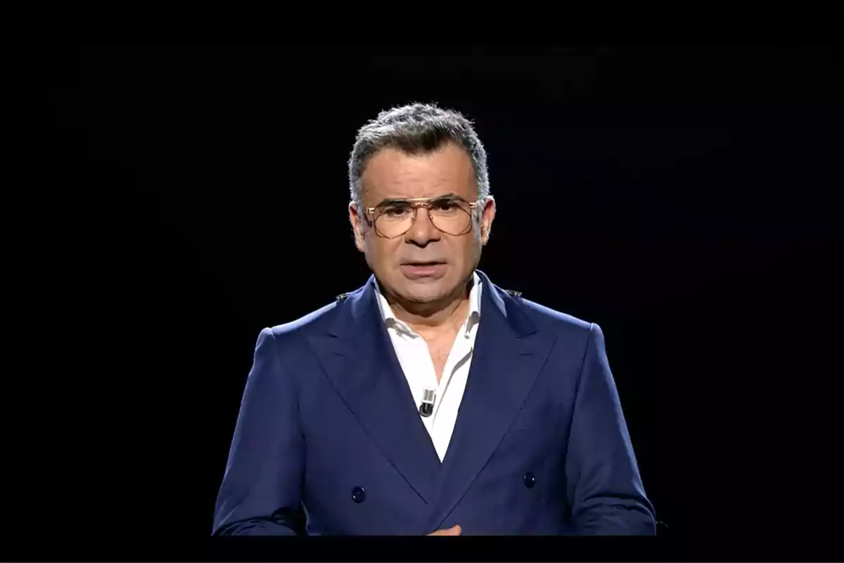 Jorge Javier Vázquez con gafas y traje azul oscuro sobre un fondo negro. Captura de 'Gran Hermano'