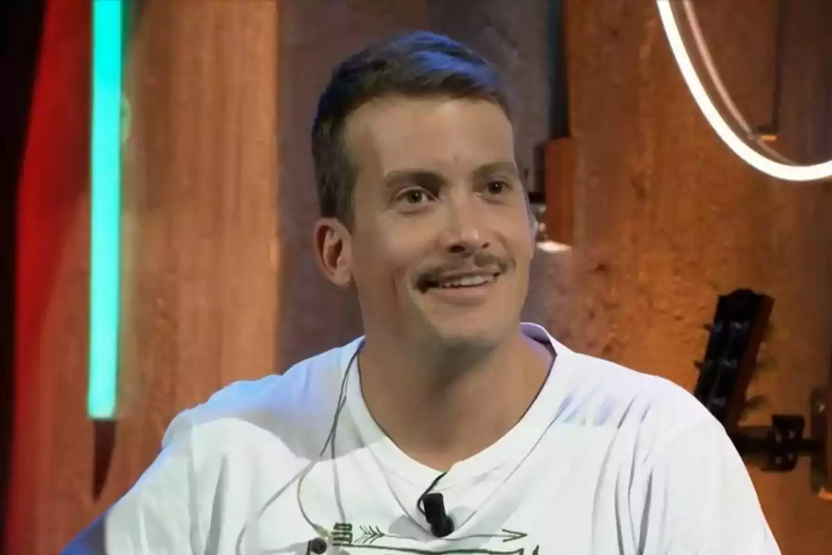 Plano corto de Grisón con bigote sonríe mientras está sentado en un ambiente con luces de colores. Plano corto de Grisón con bigote sonríe mientras está sentado en un ambiente con luces de colores.