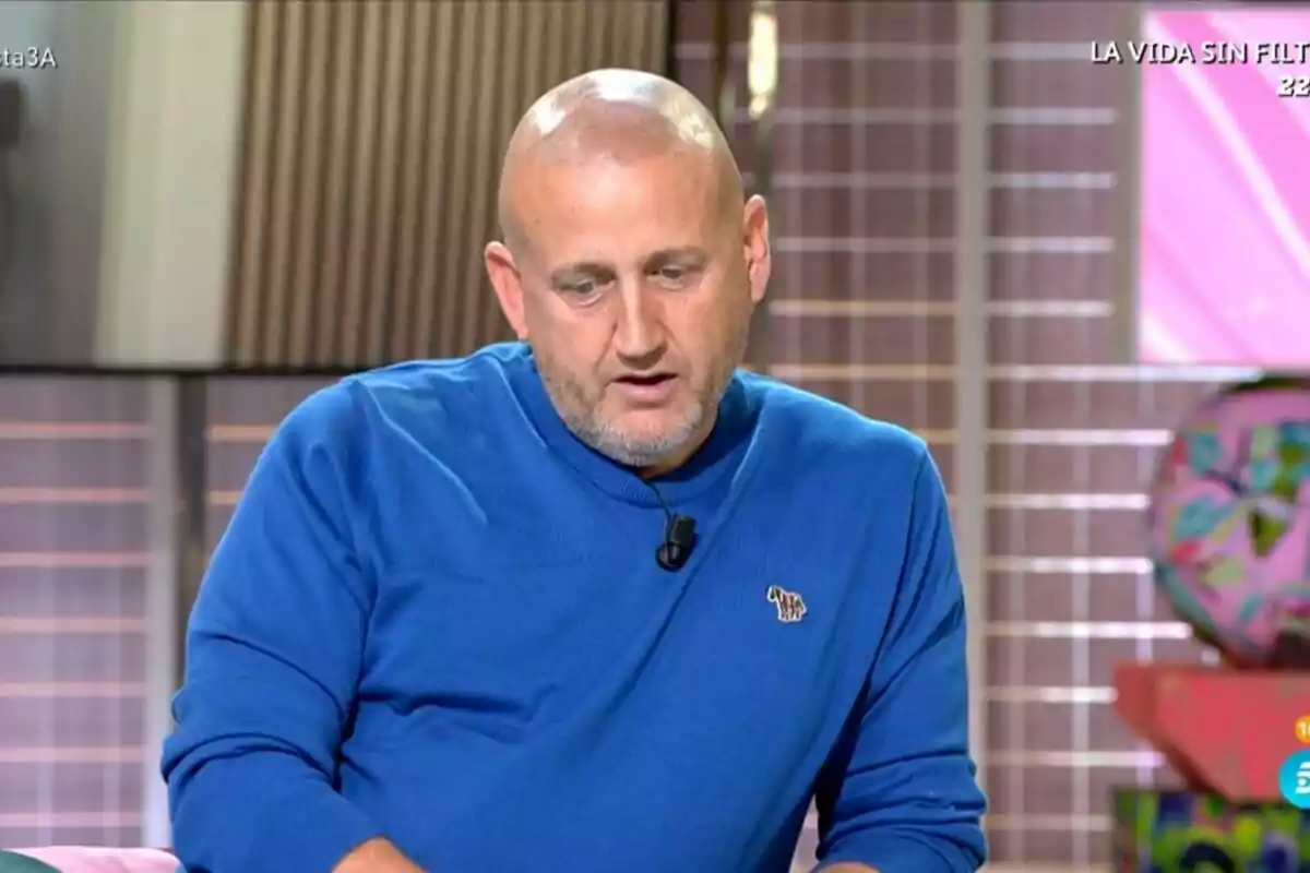 Captura de Gustavo Guillermo calvo con barba corta y camiseta azul está sentado y mirando hacia abajo en el plató de Fiesta Captura de Gustavo Guillermo calvo con barba corta y camiseta azul está sentado y mirando hacia abajo en el plató de Fiesta