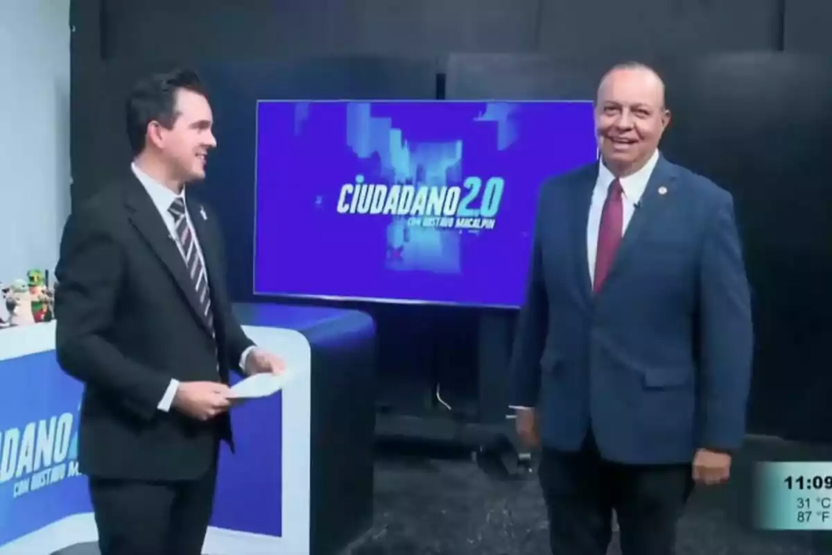 Gustavo Macalpín y Luis Arnoldo Cabada en un set de televisión con un fondo que muestra el título Gustavo Macalpín y Luis Arnoldo Cabada en un set de televisión con un fondo que muestra el título