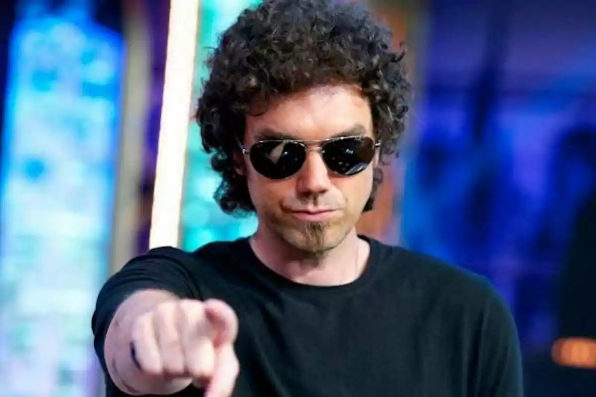Pablo Ibáñez, conocido por El hombre de negro, con gafas de sol y cabello rizado señalando hacia la cámara en un entorno colorido en El Hormiguero. Pablo Ibáñez, conocido por El hombre de negro, con gafas de sol y cabello rizado señalando hacia la cámara en un entorno colorido en El Hormiguero.