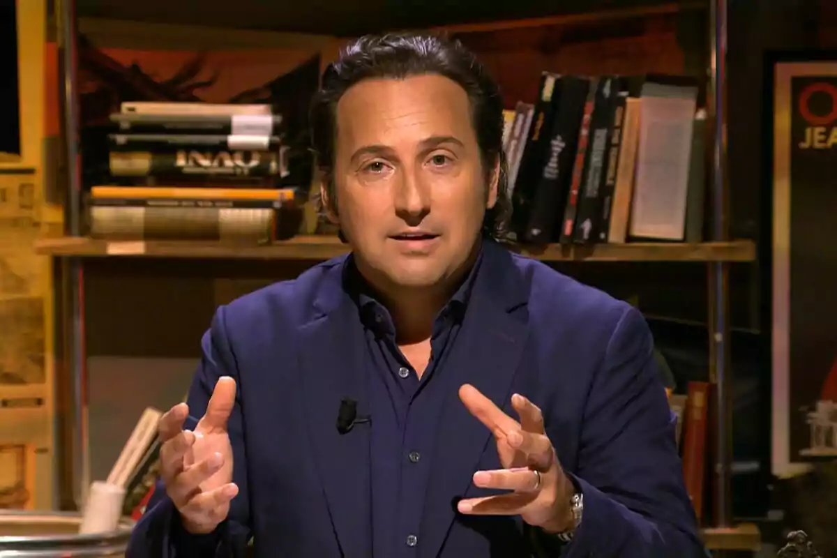 Captura d'Iker Jiménez amb vestit blau fosc està parlant i gesticulant amb les mans, mentre està assegut davant d'una prestatgeria plena de llibres al final de Quart Mil·lenni Captura d'Iker Jiménez amb vestit blau fosc està parlant i gesticulant amb les mans, mentre està assegut davant d'una prestatgeria plena de llibres al final de Quart Mil·lenni