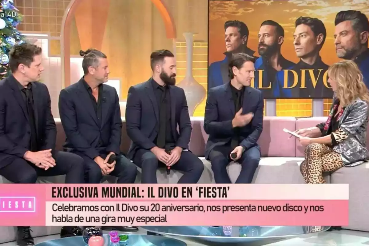 Un grupo de hombres vestidos de traje oscuro está sentado en un set de Fiesta junto a Emma García, con un cartel de fondo que dice Un grupo de hombres vestidos de traje oscuro está sentado en un set de Fiesta junto a Emma García, con un cartel de fondo que dice