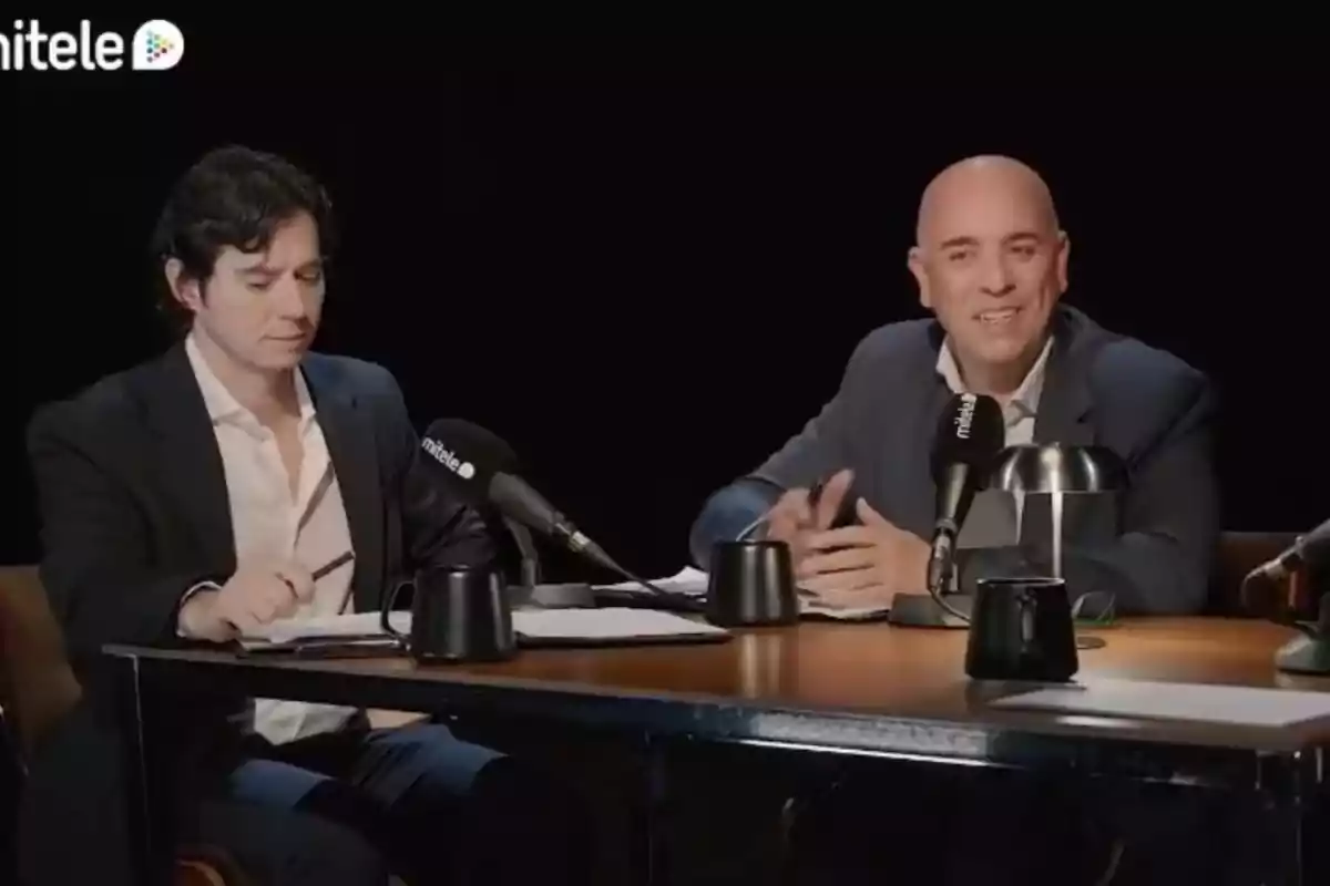 Álvaro Rojo Quintana y su compañero sentados en una mesa con micrófonos y tazas, participando en una conversación o entrevista en un estudio con fondo negro. Álvaro Rojo Quintana y su compañero sentados en una mesa con micrófonos y tazas, participando en una conversación o entrevista en un estudio con fondo negro.